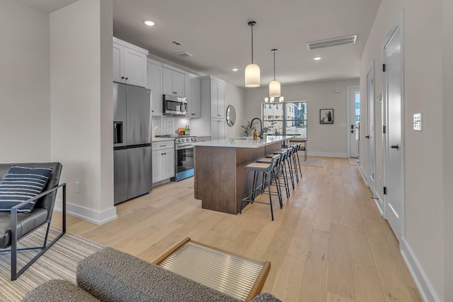 kitchen featuring white cabinetry, appliances with stainless steel finishes, decorative light fixtures, and a kitchen island with sink