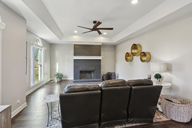 living room with ceiling fan, dark hardwood / wood-style floors, a fireplace, and a tray ceiling