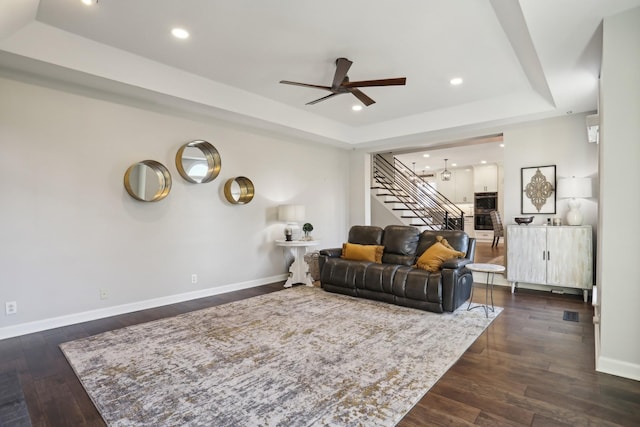 living room with dark wood-type flooring, ceiling fan, and a raised ceiling