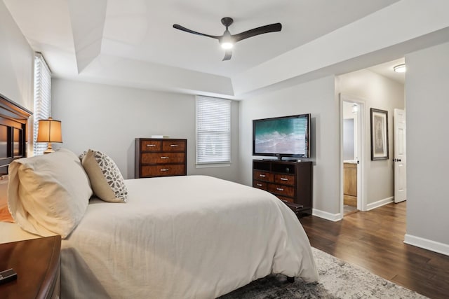 bedroom with dark wood-type flooring, ensuite bath, a tray ceiling, and multiple windows