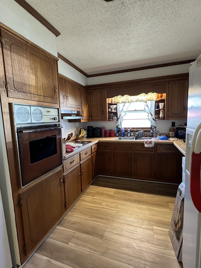 kitchen with wall oven, sink, ornamental molding, and a textured ceiling