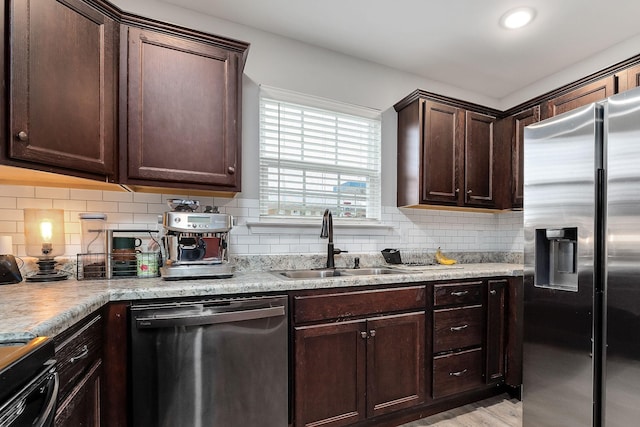 kitchen with dark brown cabinetry, sink, stainless steel appliances, light hardwood / wood-style floors, and decorative backsplash