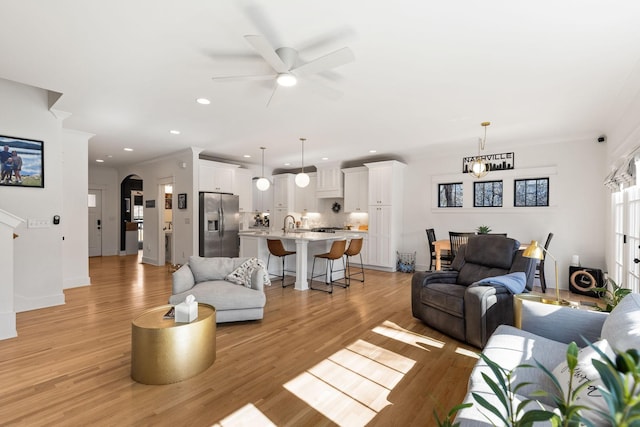 living room with sink, crown molding, ceiling fan, and light wood-type flooring