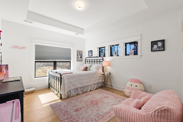 bedroom with light hardwood / wood-style flooring and a tray ceiling