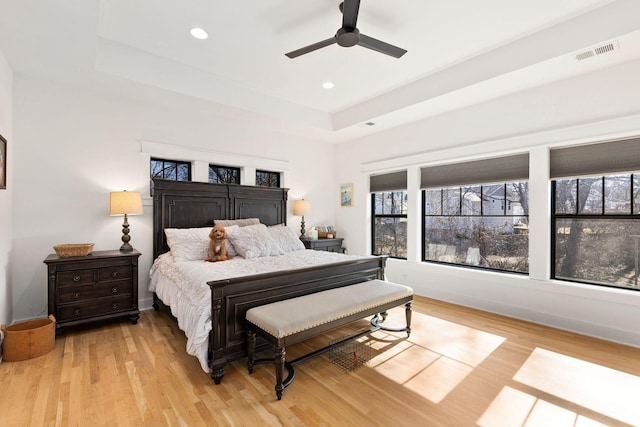 bedroom with ceiling fan, a tray ceiling, and light wood-type flooring