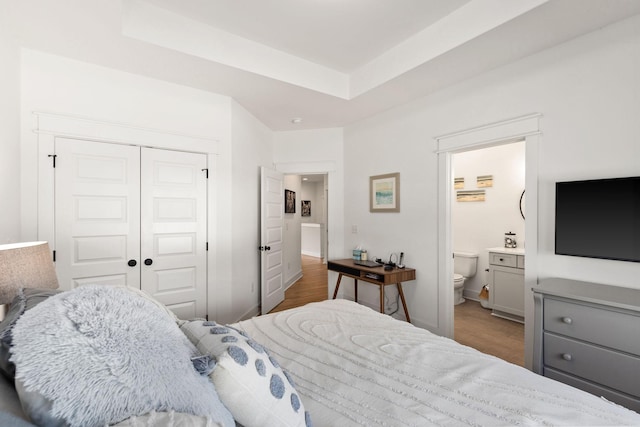 bedroom with a closet, dark wood-type flooring, a raised ceiling, and ensuite bathroom