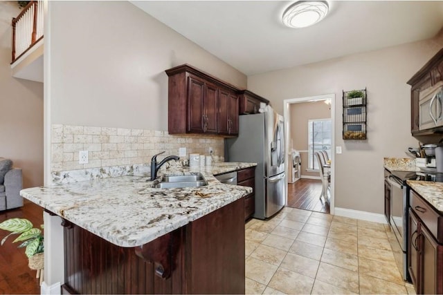 kitchen featuring sink, appliances with stainless steel finishes, a kitchen breakfast bar, kitchen peninsula, and light stone countertops