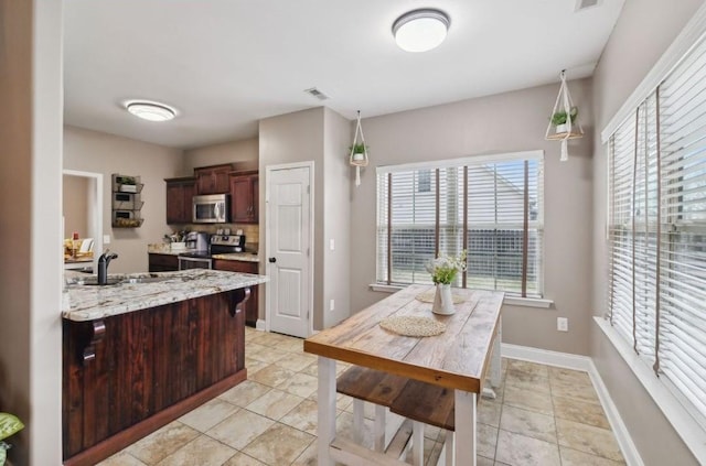 kitchen with light tile patterned flooring, sink, pendant lighting, stainless steel appliances, and light stone countertops