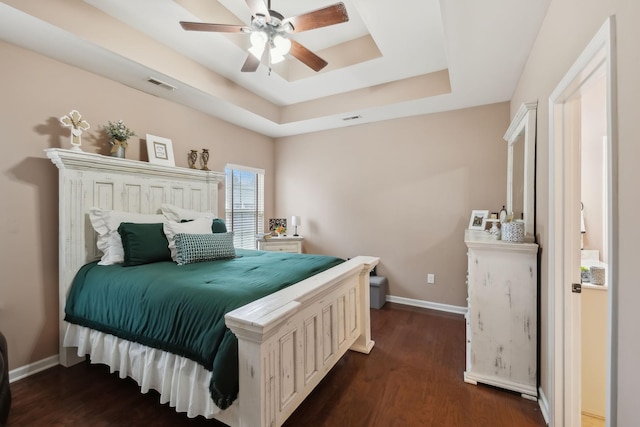 bedroom with dark hardwood / wood-style floors, ceiling fan, and a tray ceiling