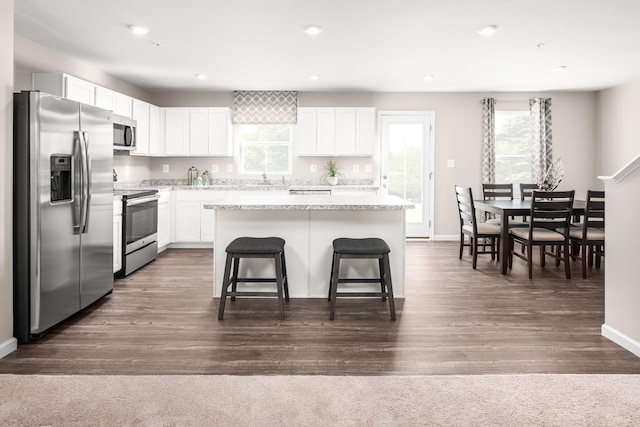 kitchen featuring appliances with stainless steel finishes, white cabinetry, a kitchen bar, a center island, and dark wood-type flooring