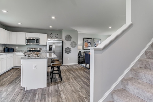 kitchen featuring a kitchen bar, light stone counters, a kitchen island, stainless steel appliances, and white cabinets