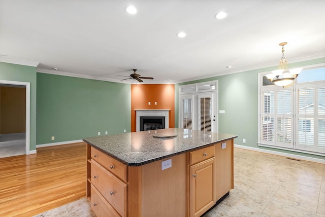 kitchen featuring ceiling fan with notable chandelier, decorative light fixtures, dark stone countertops, a center island, and crown molding