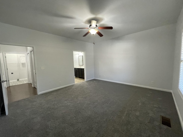 unfurnished bedroom featuring dark carpet, ensuite bath, and ceiling fan