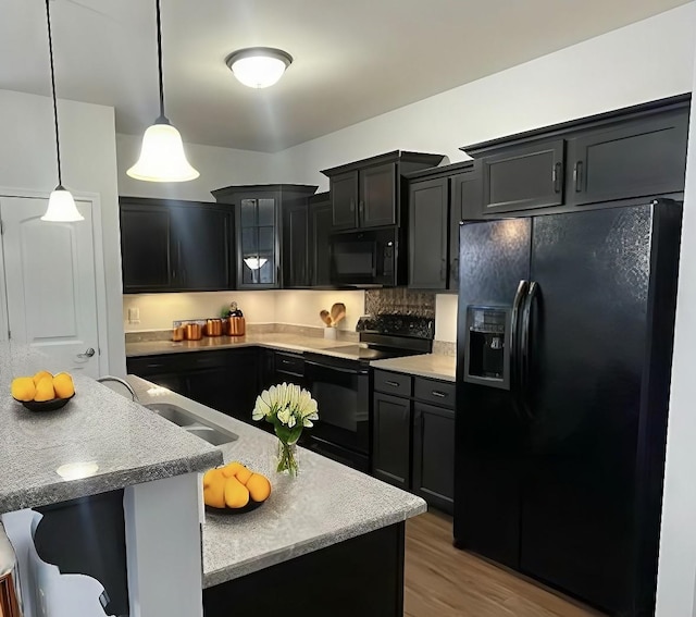 kitchen featuring sink, hanging light fixtures, a kitchen breakfast bar, black appliances, and light wood-type flooring