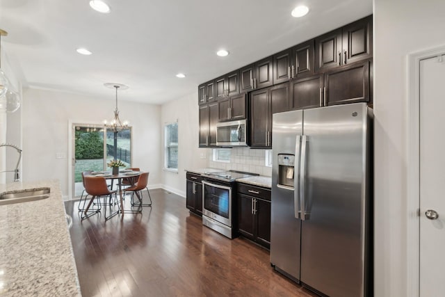 kitchen with appliances with stainless steel finishes, dark hardwood / wood-style floors, pendant lighting, sink, and light stone counters