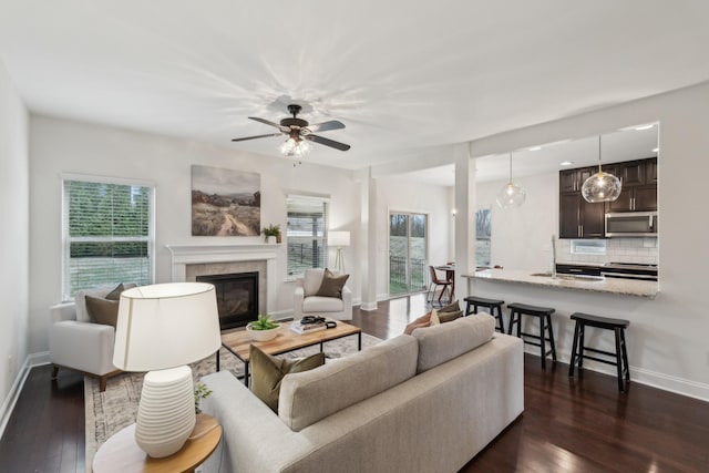 living room with ceiling fan, dark hardwood / wood-style flooring, a tiled fireplace, and sink