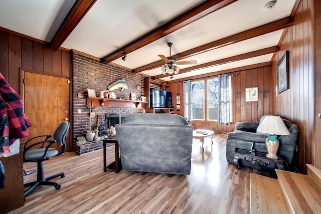 living room featuring a brick fireplace, wooden walls, beamed ceiling, and light wood-type flooring