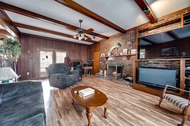 living room with ceiling fan, a brick fireplace, light wood-type flooring, beamed ceiling, and wood walls