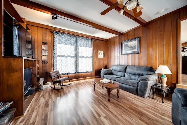 living room featuring hardwood / wood-style flooring, wooden walls, beam ceiling, and ceiling fan