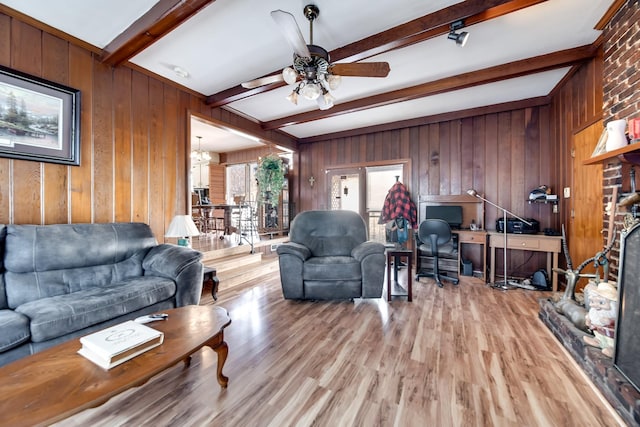 living room featuring ceiling fan with notable chandelier, wood walls, beam ceiling, and light hardwood / wood-style floors