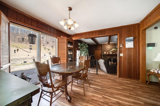 dining area with hardwood / wood-style floors, wood walls, a chandelier, and a brick fireplace