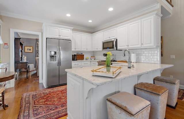 kitchen with a kitchen bar, white cabinetry, light stone counters, kitchen peninsula, and stainless steel appliances