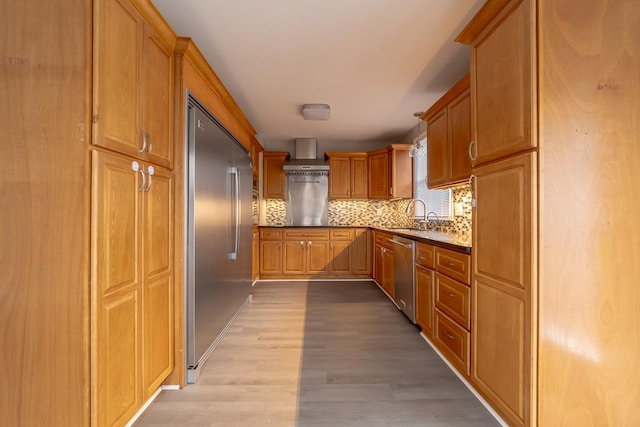 kitchen featuring wall chimney range hood, sink, appliances with stainless steel finishes, tasteful backsplash, and light hardwood / wood-style floors