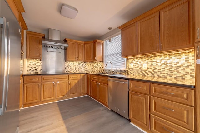 kitchen featuring decorative light fixtures, sink, stainless steel appliances, wall chimney range hood, and light wood-type flooring