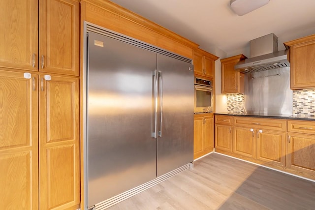 kitchen with stainless steel appliances, wall chimney range hood, backsplash, and light hardwood / wood-style flooring