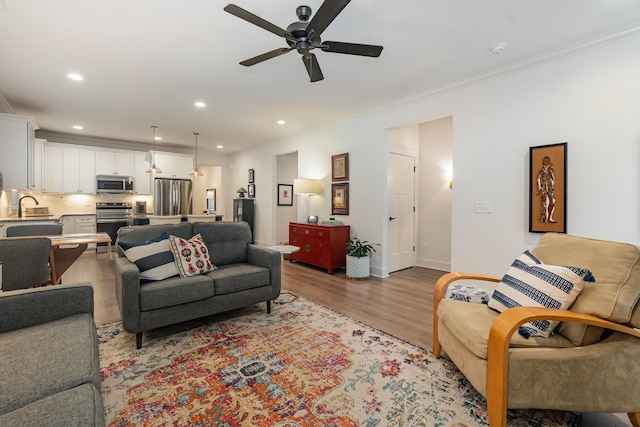 living room with hardwood / wood-style flooring, ceiling fan, ornamental molding, and sink