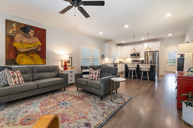 living room featuring dark hardwood / wood-style flooring, sink, ornamental molding, and ceiling fan