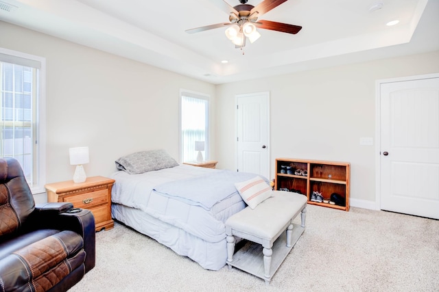 bedroom with a tray ceiling, light colored carpet, and ceiling fan