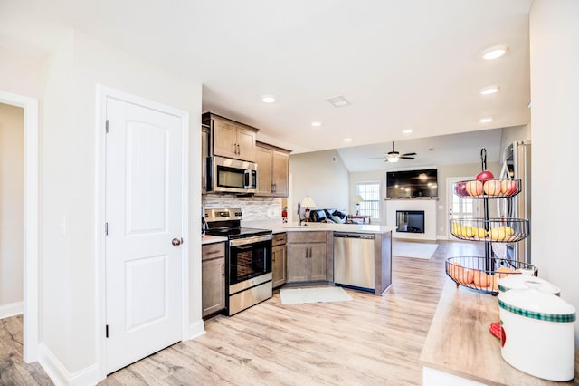 kitchen with ceiling fan, appliances with stainless steel finishes, backsplash, light hardwood / wood-style floors, and kitchen peninsula