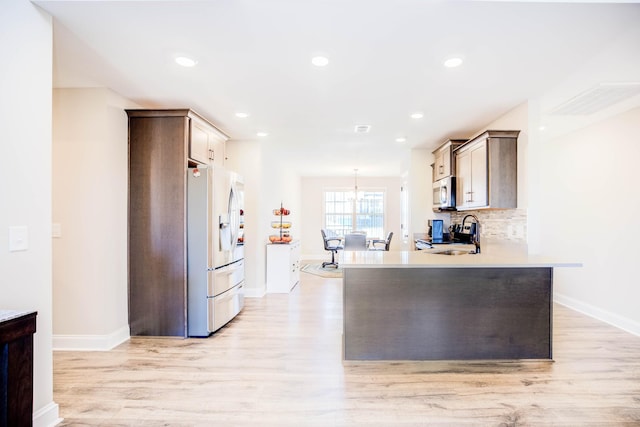 kitchen featuring sink, light hardwood / wood-style flooring, appliances with stainless steel finishes, backsplash, and kitchen peninsula