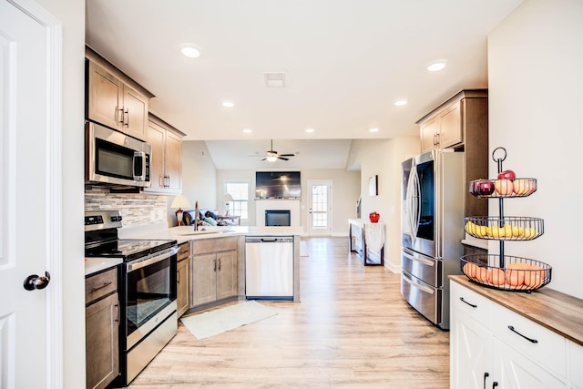 kitchen featuring sink, tasteful backsplash, light hardwood / wood-style flooring, ceiling fan, and stainless steel appliances