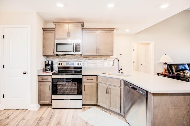 kitchen with appliances with stainless steel finishes, sink, decorative backsplash, kitchen peninsula, and light hardwood / wood-style flooring