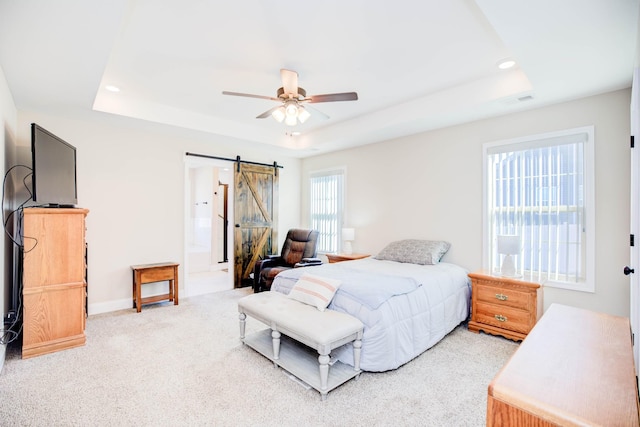 carpeted bedroom with ceiling fan, a barn door, and a raised ceiling