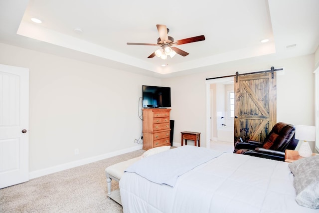 carpeted bedroom featuring a barn door, ceiling fan, and a tray ceiling