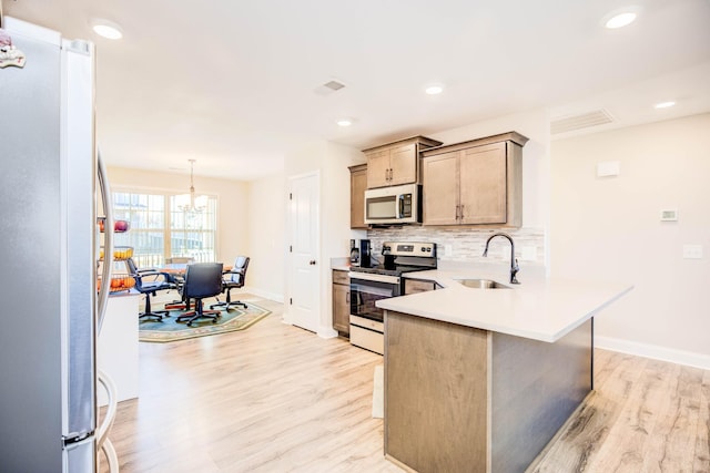 kitchen with pendant lighting, sink, light hardwood / wood-style flooring, appliances with stainless steel finishes, and decorative backsplash