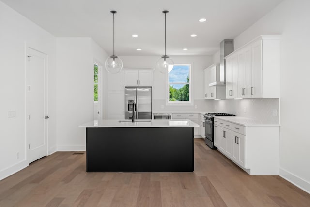 kitchen featuring appliances with stainless steel finishes, pendant lighting, white cabinetry, a kitchen island with sink, and wall chimney exhaust hood