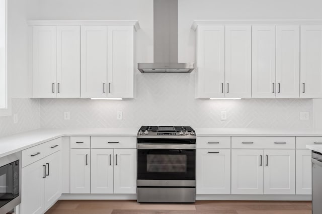 kitchen with appliances with stainless steel finishes, wall chimney range hood, white cabinets, and decorative backsplash