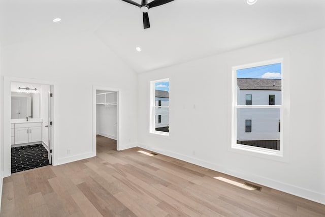 unfurnished bedroom with ensuite bathroom, a spacious closet, light wood-type flooring, a closet, and ceiling fan