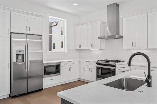 kitchen featuring sink, white cabinetry, light hardwood / wood-style flooring, appliances with stainless steel finishes, and wall chimney range hood