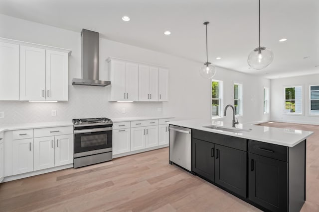 kitchen featuring appliances with stainless steel finishes, white cabinetry, sink, hanging light fixtures, and wall chimney range hood