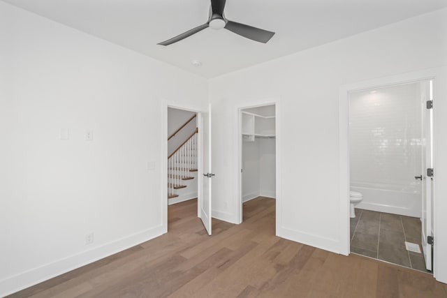 unfurnished bedroom featuring ensuite bathroom, hardwood / wood-style floors, a walk in closet, ceiling fan, and a closet