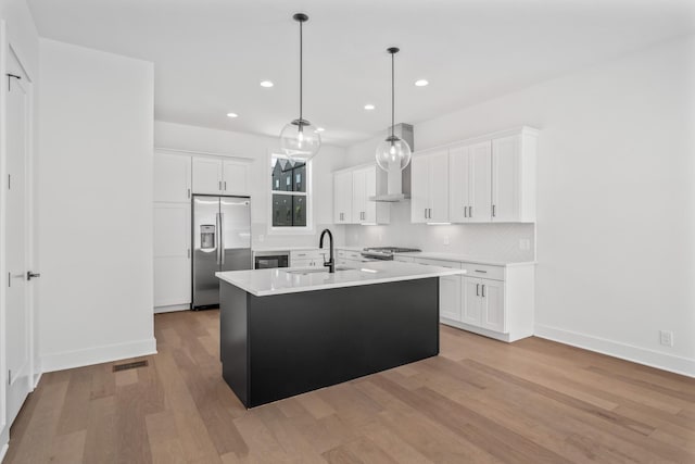 kitchen with sink, a kitchen island with sink, stainless steel appliances, white cabinets, and decorative light fixtures