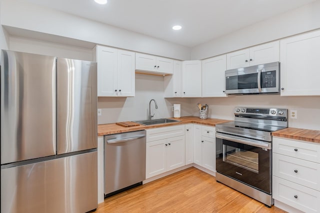 kitchen featuring appliances with stainless steel finishes, butcher block countertops, sink, white cabinets, and light hardwood / wood-style flooring