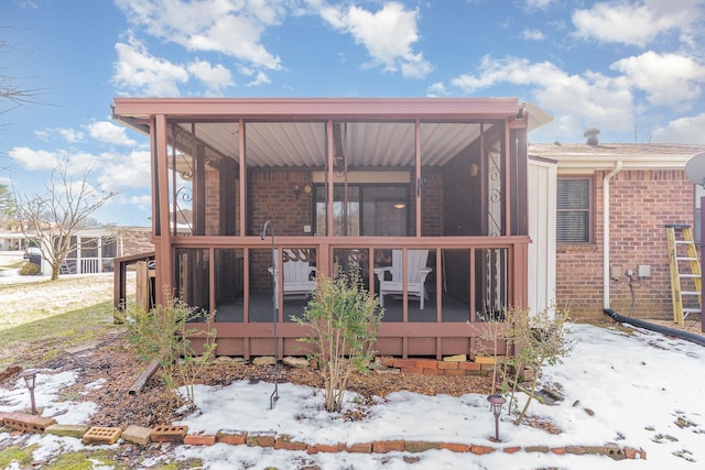 snow covered back of property featuring a sunroom