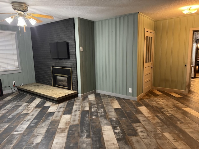 unfurnished living room with wood walls, a brick fireplace, a textured ceiling, dark hardwood / wood-style flooring, and ceiling fan