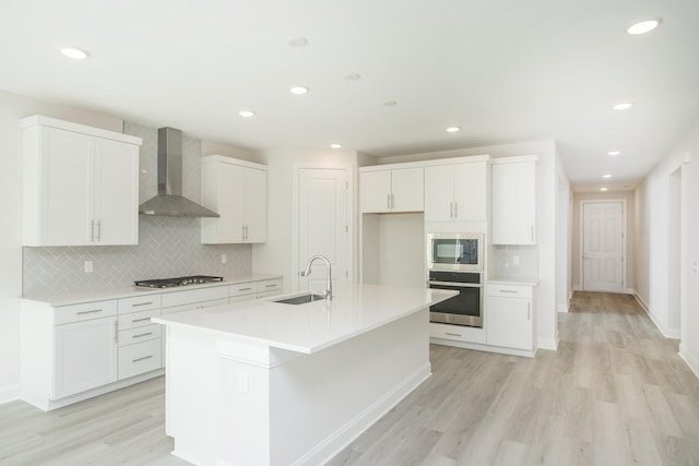 kitchen featuring sink, white cabinetry, stainless steel oven, built in microwave, and wall chimney exhaust hood